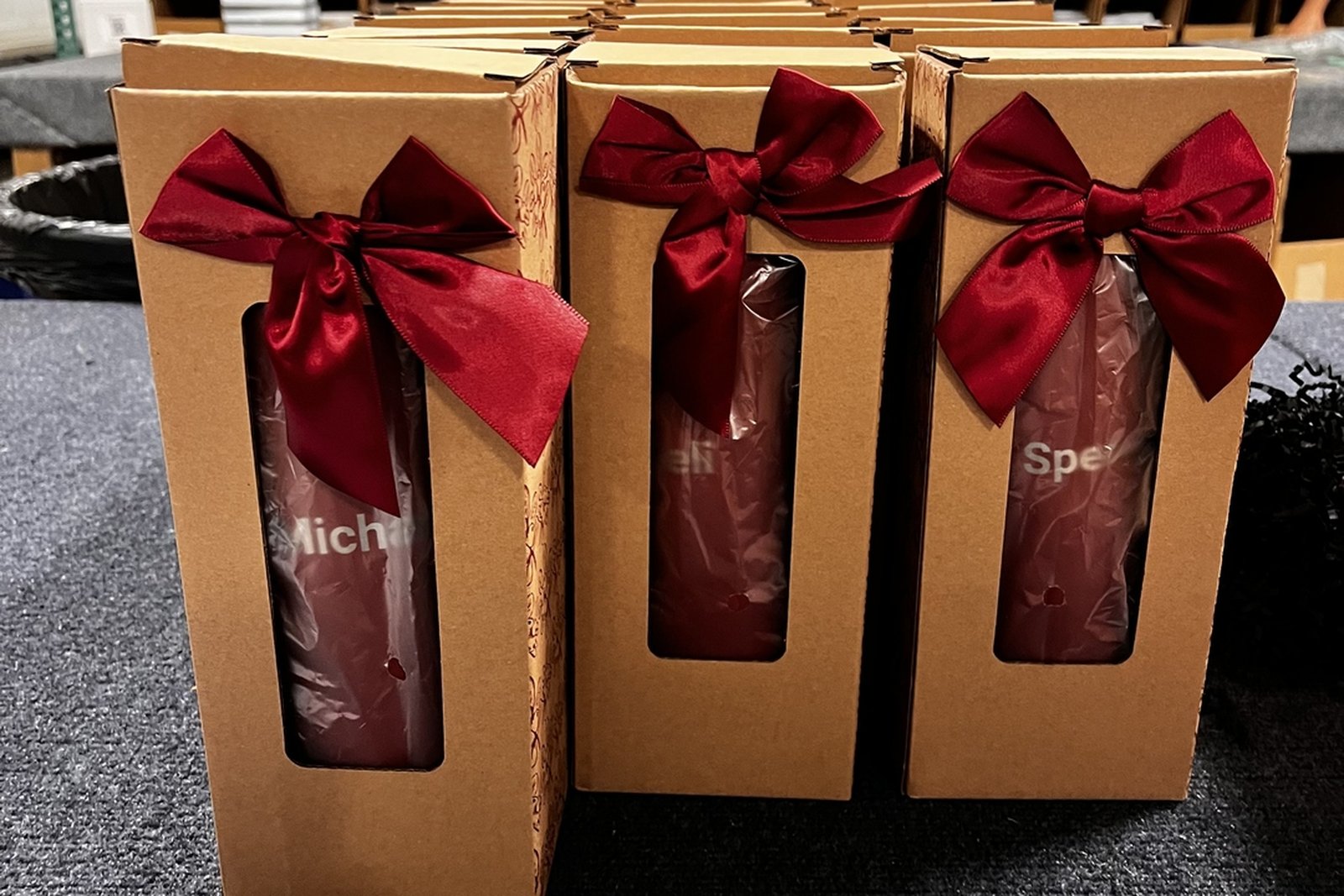 Personalized tumblers in gift boxes with red bows ready for a corporate holiday program